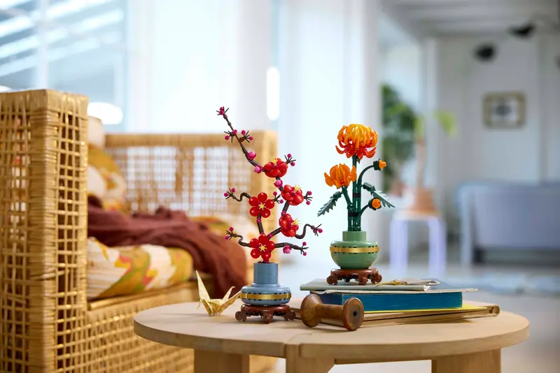 LEGO Botanical Collection Plum Blossom 10369 and Chrysanthemum 10368 displayed on a round coffee table in a cozy living room