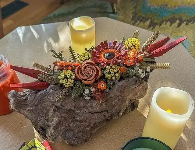 Custom LEGO autumn centerpiece by @chicagobud featuring orange, red, and yellow flowers arranged on a driftwood base surrounded by candles.