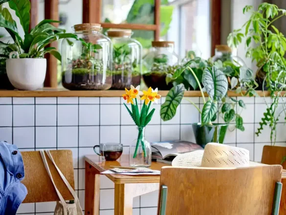 LEGO Daffodils 40747 displayed in a clear glass vase on a cozy wooden table surrounded by indoor plants
