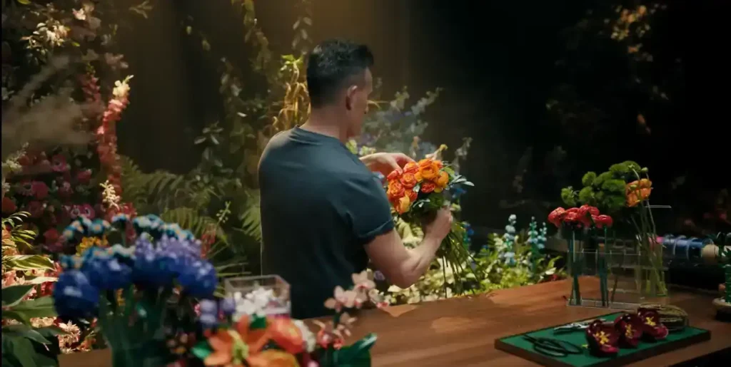 LEGO designer holding the Persian buttercup build from the LEGO Pretty Pink Flower Bouquet 10342, surrounded by other LEGO Botanical Collection flowers