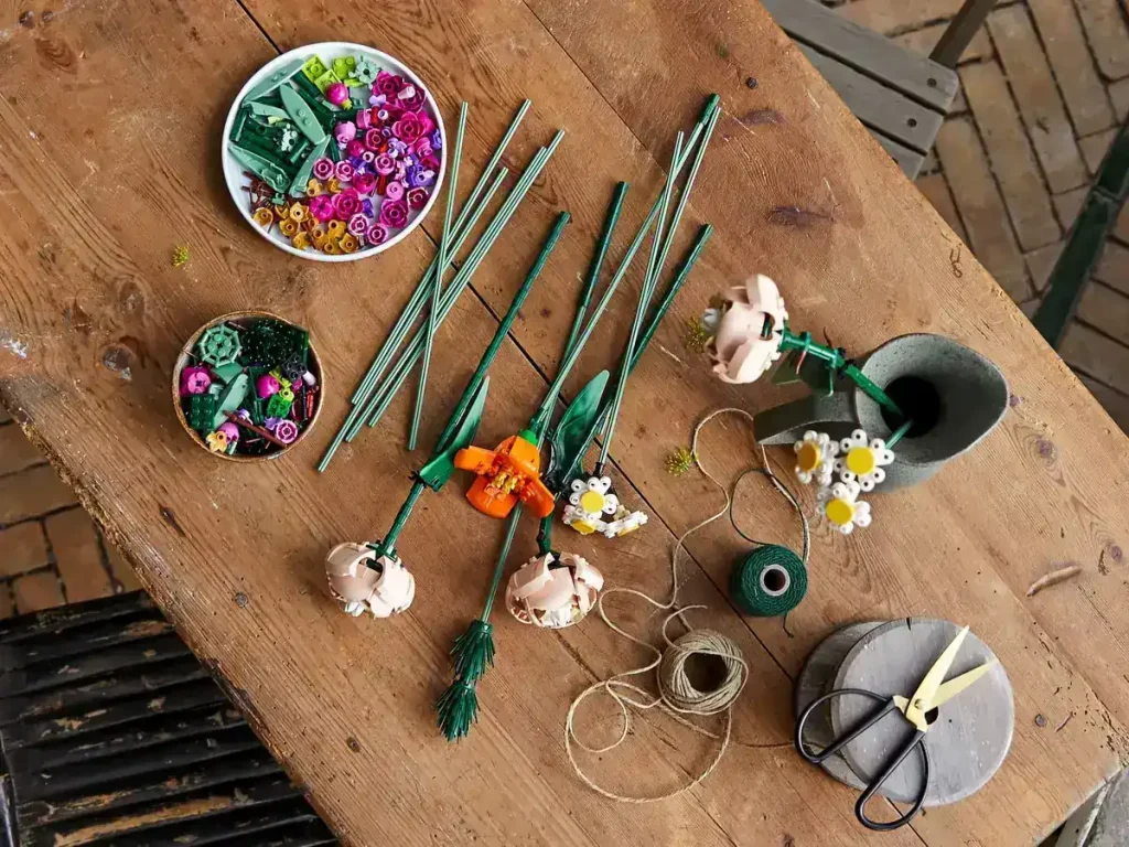 LEGO flower pieces, stems, and petals laid out on a wooden table with tools and string.