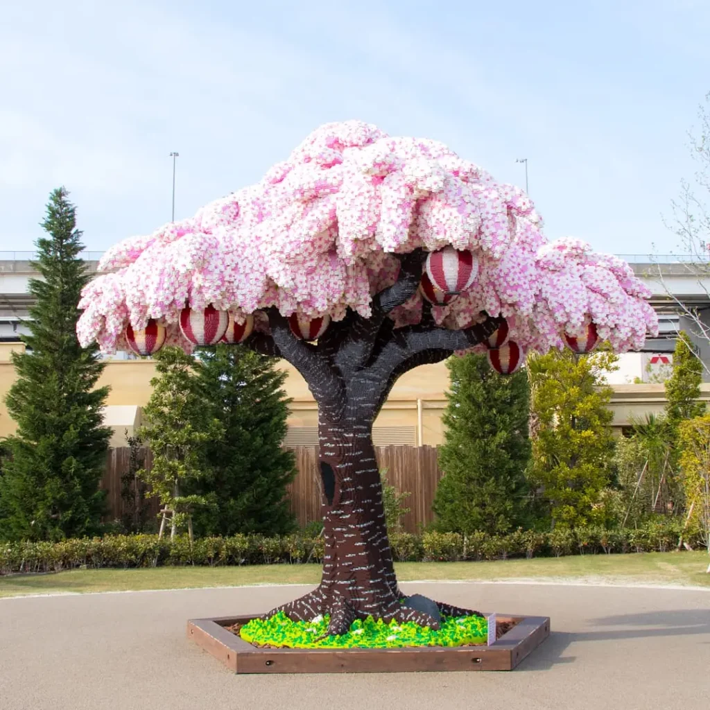 LEGO cherry blossom tree at LEGOLAND Japan featuring pink sakura-style blossoms, hanging lanterns, and a dark brick trunk on a landscaped base.