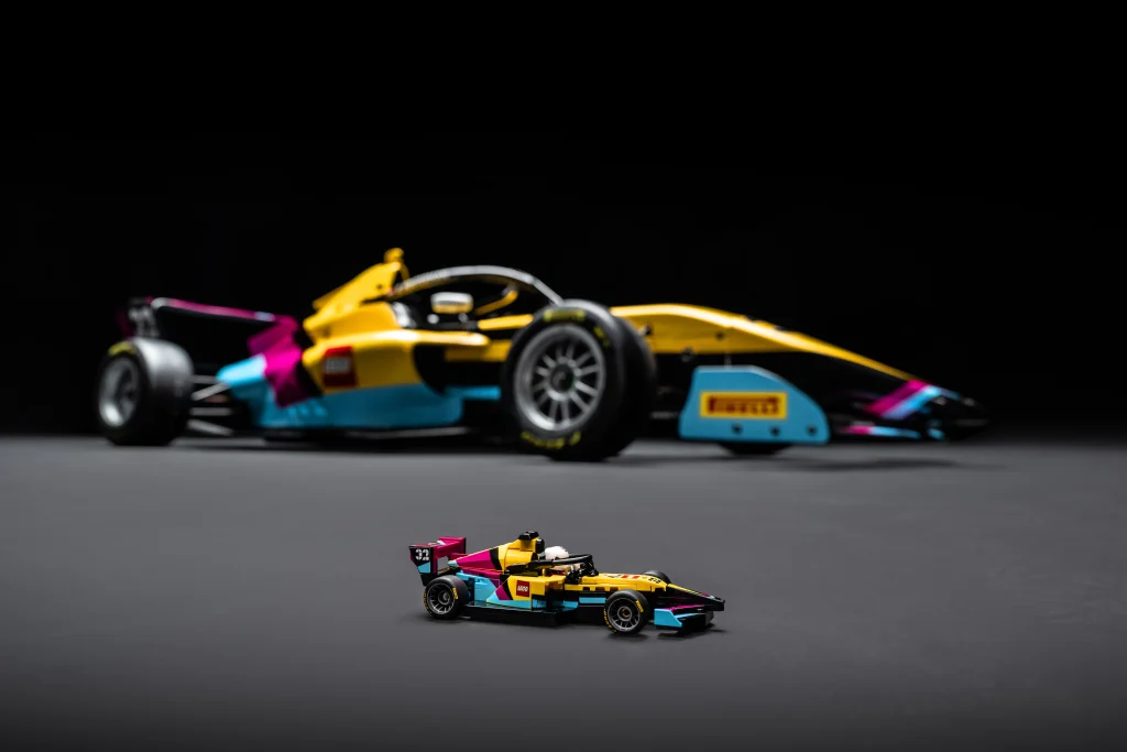 Mini LEGO F1 Academy race car model displayed in front of the full-scale 2025 LEGO livery F1 car, shown in a dark studio setting.