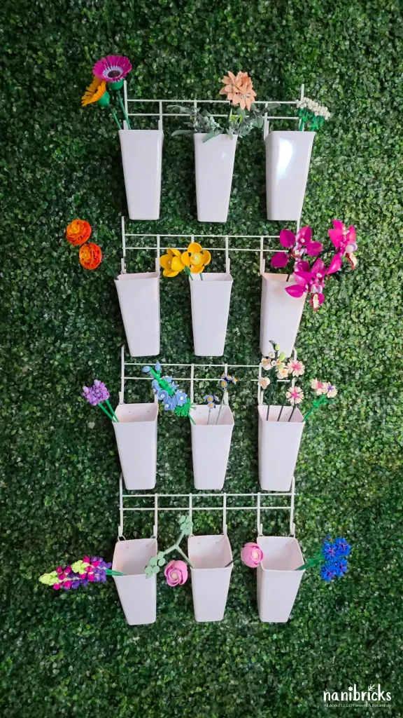 Nanibricks DIY LEGO Botanicals flower bar made with white hanging vases, displaying assorted LEGO flower stems organized by color on a green studio wall.