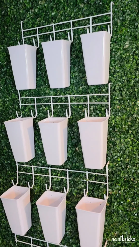 Finished DIY LEGO Botanicals flower bar with white plastic vases mounted on over-the-door hook racks against a green wall.