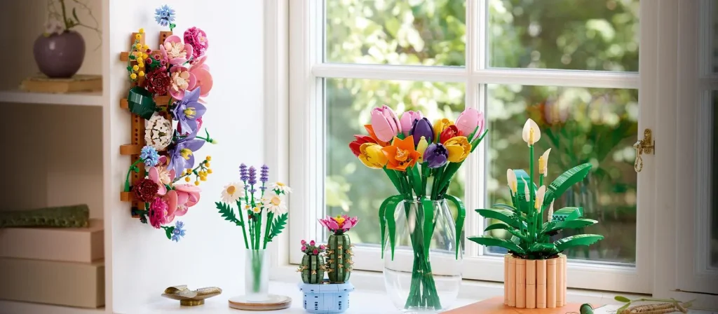 LEGO Botanicals sets displayed on a windowsill, including flower bouquets, a cactus, and a potted peace lily in a bright home setting.