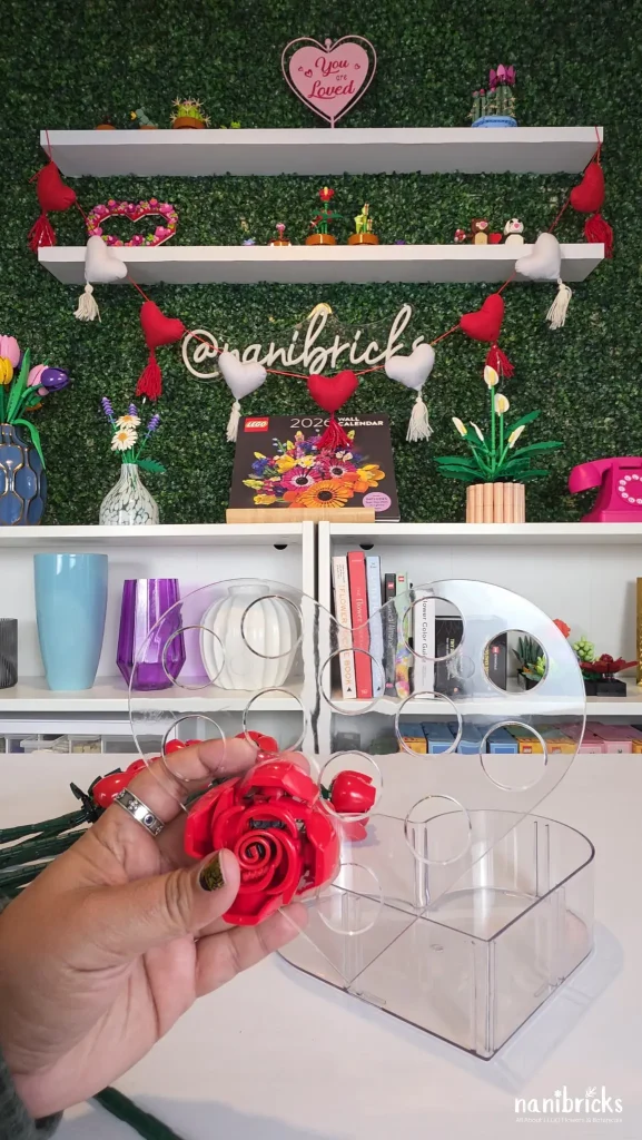 LEGO rose positioned near the openings of a heart-shaped vase while planning flower placement.