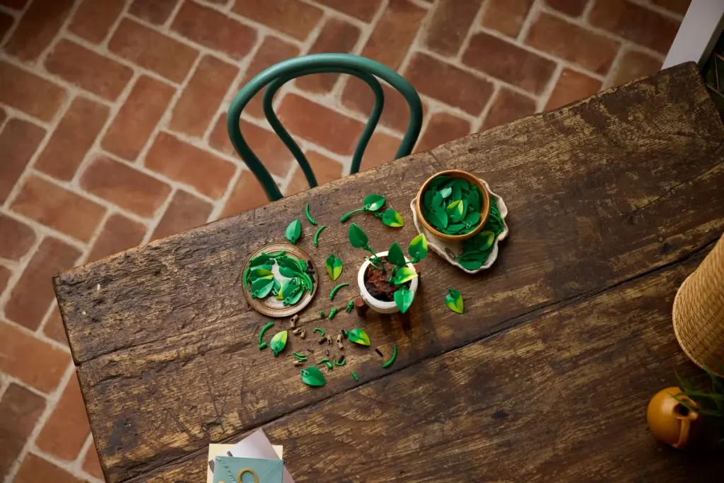 LEGO Botanicals Hanging Golden Pothos (11512) partially assembled on a wooden table with leaves, vines, and plant elements spread out during the build process.