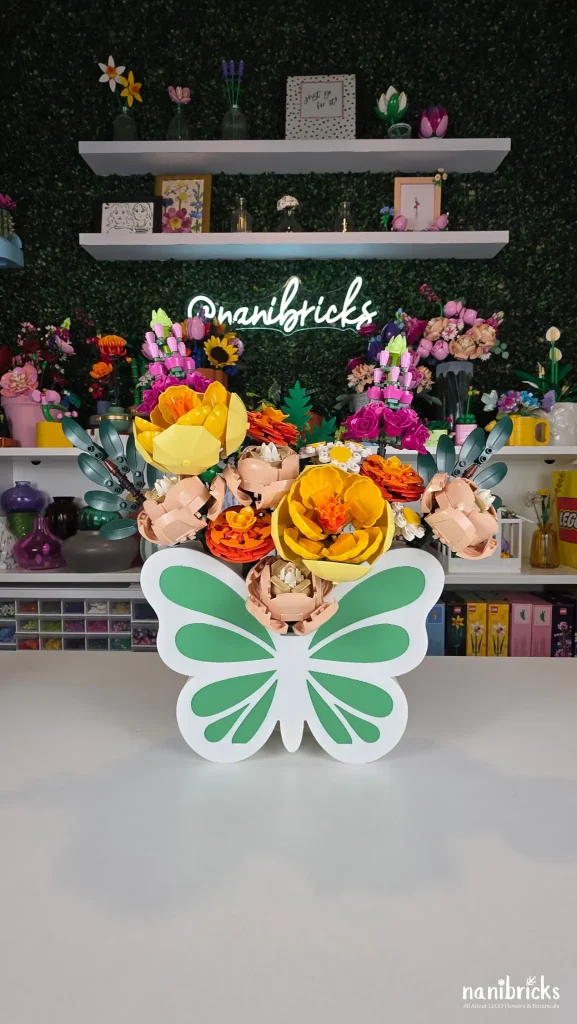 Completed Butterfly Meadow LEGO flower arrangement displayed in a butterfly vase on a tabletop with colorful LEGO Botanicals in the background.