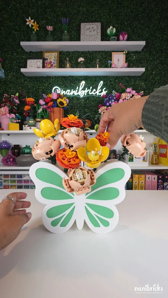 Adding orange ranunculus around the yellow peonies and peach roses while building the Butterfly Meadow LEGO flower arrangement.