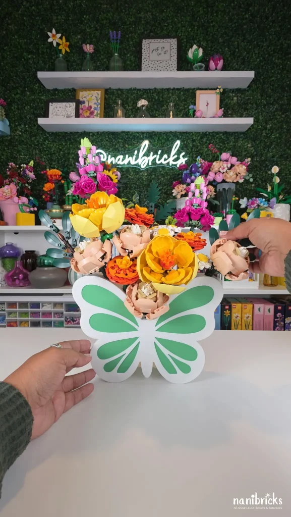 Adding greenery branches and daisy leaves to frame the Butterfly Meadow LEGO flower arrangement in a butterfly vase.