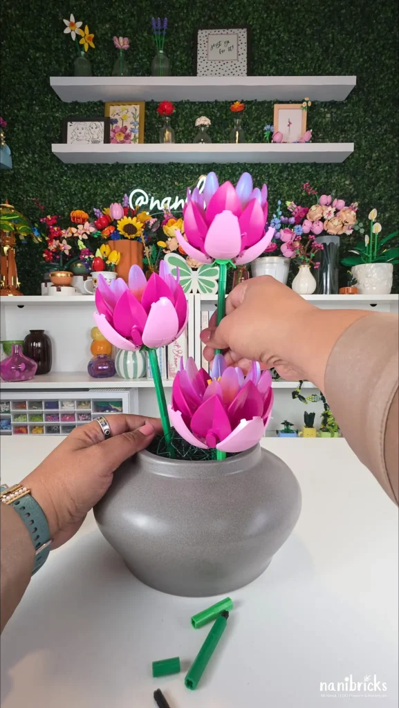 Three pink LEGO Water Lilies being positioned at different heights in a gray vase